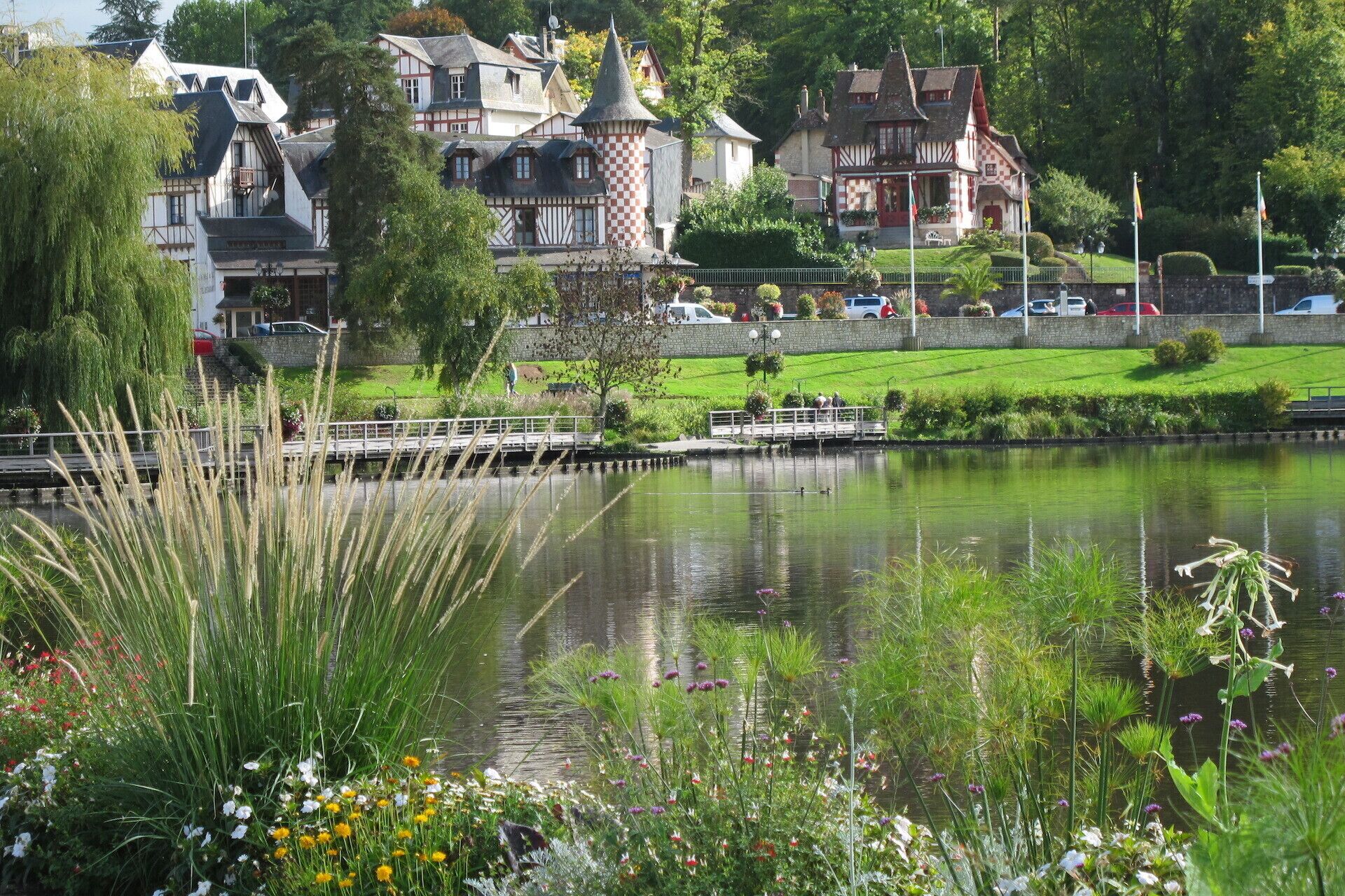 A riverside view with traditional buildings, a bridge, and a grassy area with flowers.