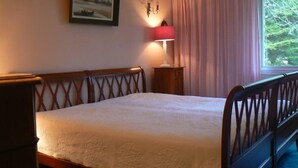 Une chambre à coucher avec un lit en bois, une table de chevet avec une lampe, une fenêtre avec des rideaux et un tableau encadré au mur.