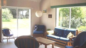Une pièce baignée de lumière, avec un canapé bleu, deux fauteuils et une table basse en bois.
