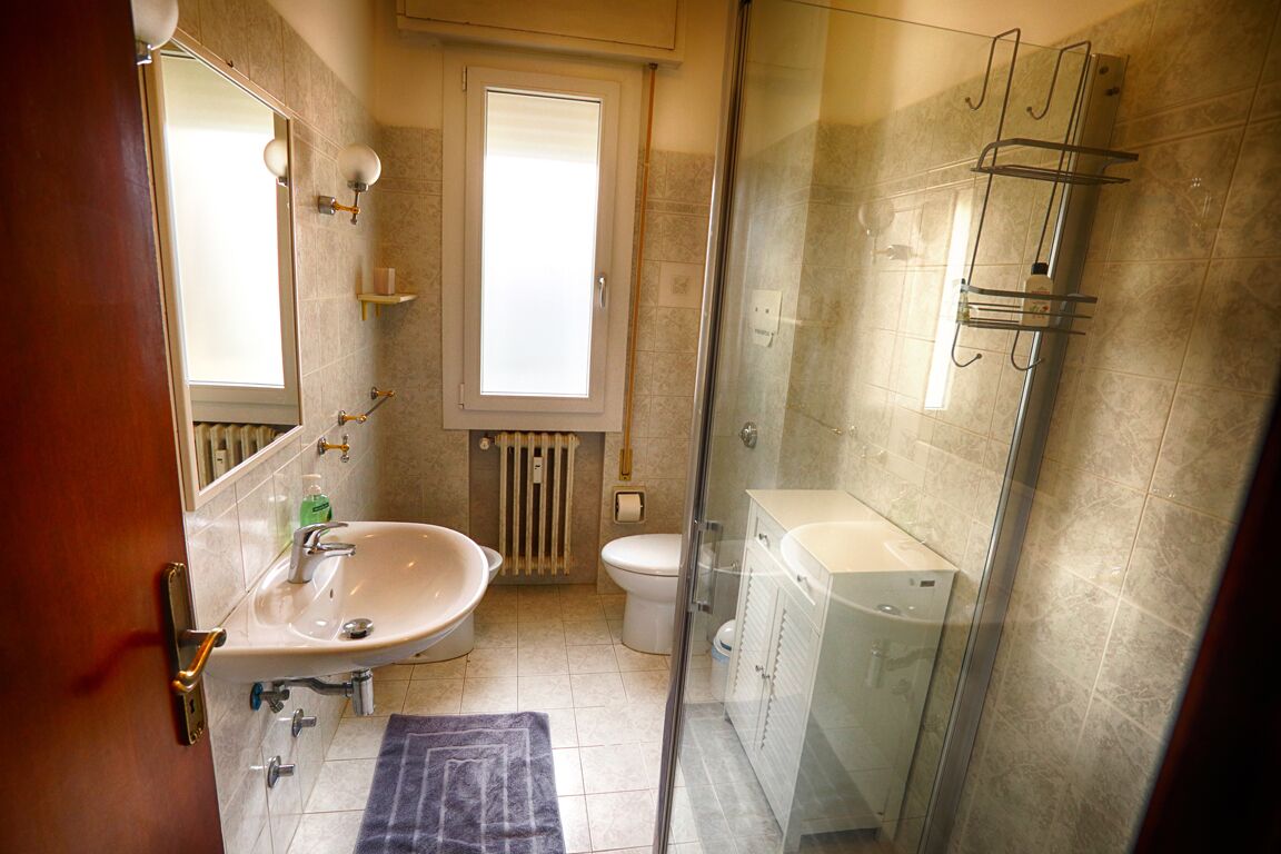 Een badkamer met een douchecabine van glas, een wastafel, een toilet en een raam.