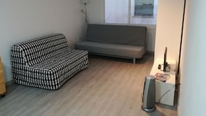 Une petite pièce au mobilier minimaliste, avec un canapé à motifs, un canapé uni de couleur grise et un lampadaire.