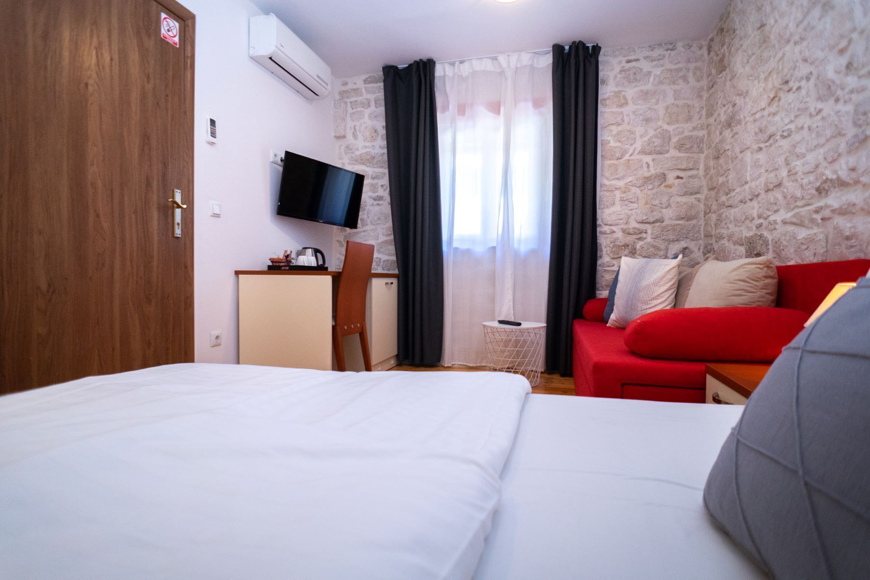 Habitación de hotel con cama, escritorio con televisor, sofá rojo y pared de piedra.
