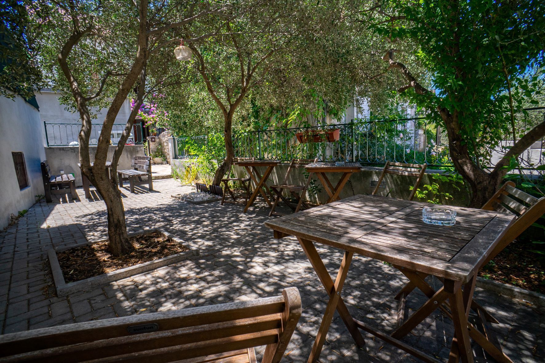Eine Terrasse im Freien mit Holztischen und -bänken, umgeben von Bäumen und einem Pflasterweg.