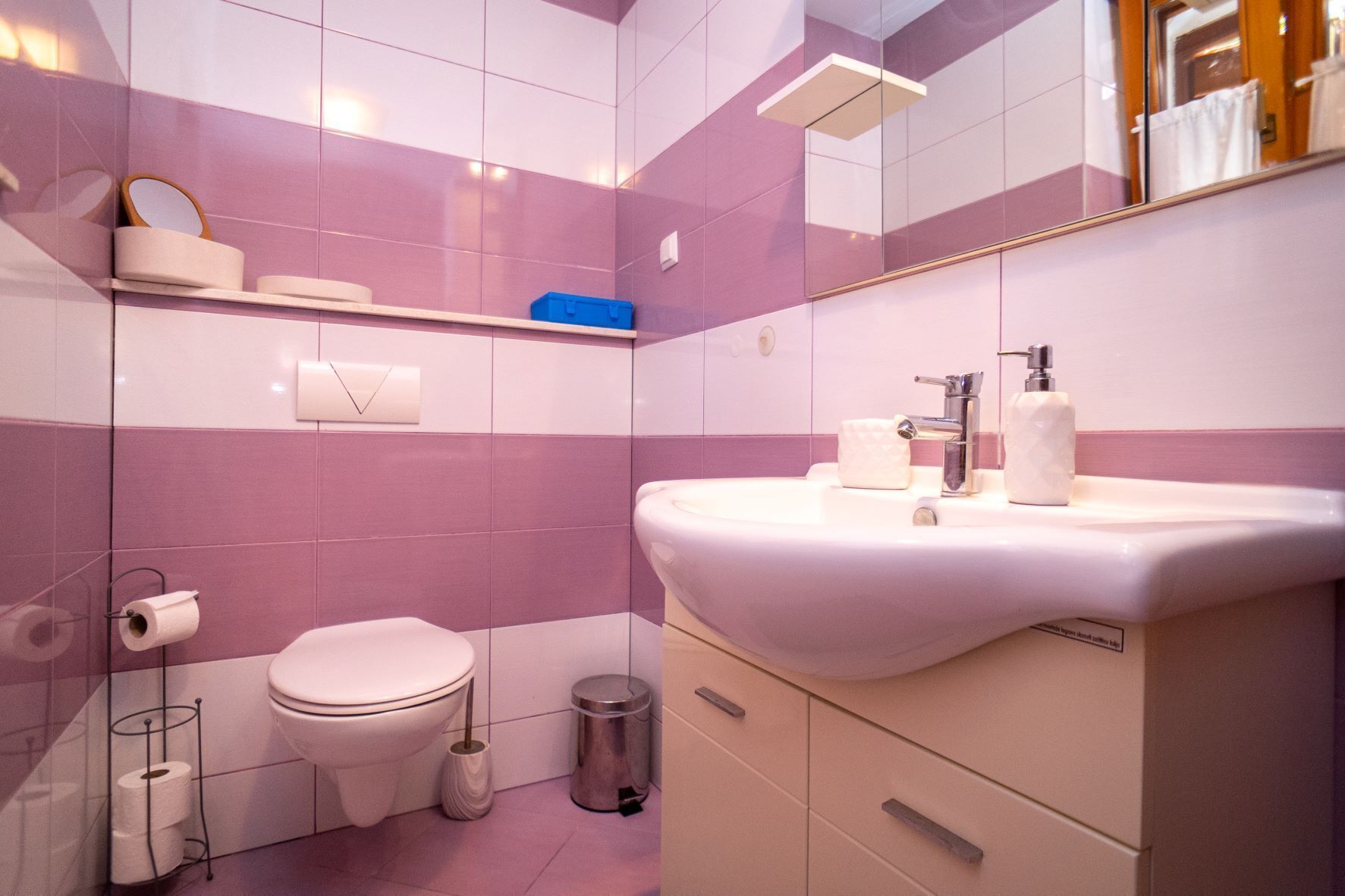 Un baño moderno con un lavamanos blanco, un inodoro y un espejo sobre el lavamanos.