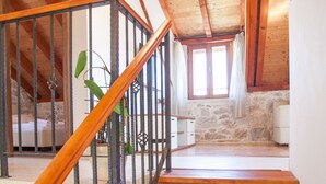 Una escalera de madera con barandales de metal que conduce a una habitación con paredes de piedra y un ventanal con cortinas.