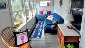 Ein gemütliches Zimmer mit einem blauen Sofa, einem Holzstuhl, einem kleinen Tisch und einem Deckenventilator.