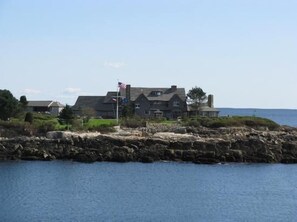 A large, two-story stone house with a flagpole in front, situated on a rocky shoreline with a view of the sea. - Charming Cottage 5 min walk to beach & 8 min. walk to The Pier !!! (Old Orchard Beach)