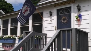 Ein weißes Cottage mit der Hausnummer 28, einer Flagge und einer Veranda mit amerikanischen Flaggen.