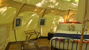 A tented room with a bed, a table with a radio and papers, and two framed pictures on the wall.