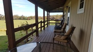 Une véranda couverte avec des balustrades en bois, une table en verre et plusieurs fauteuils rembourrés.