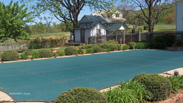 Un jardin avec une piscine, une petite maison blanche avec un toit vert et une clôture en bois.