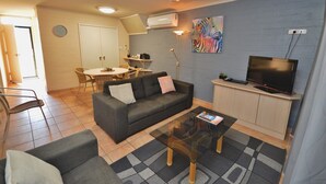 Een woonkamer met een bank, salontafel, televisie en een eethoek met stoelen en een tafel.