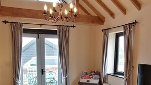 A cozy living room with a wooden ceiling, a chandelier, a sofa, a coffee table, and a view through a glass door to an outdoor area.