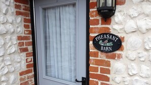 A white door with a glass panel, a black lantern, and a 'PEASANT BARN' sign on a brick wall.