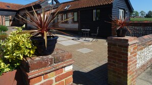 A brick patio with potted plants, a small table with chairs, and a building with a tiled roof.