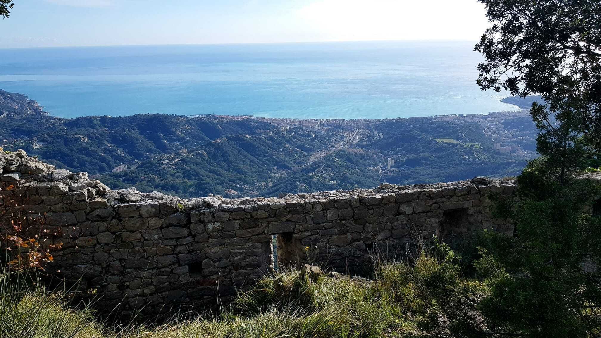 A stone wall with a view of a coastal landscape and distant city.