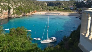 A coastal bay with boats, a sandy beach, and a rocky hillside. - Casa Llebeig - Apartament with panoramic Sea view of Cala en Porter - Menorca (Cala en Porter)