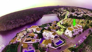 An aerial view of a coastal town with white buildings, a central road, and a body of water. - Casa Llebeig - Apartament with panoramic Sea view of Cala en Porter - Menorca (Cala en Porter)