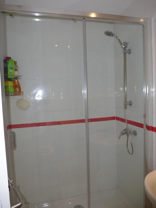 Een douchecabine met glazen wanden, een handdouche en een kraan op de muur.