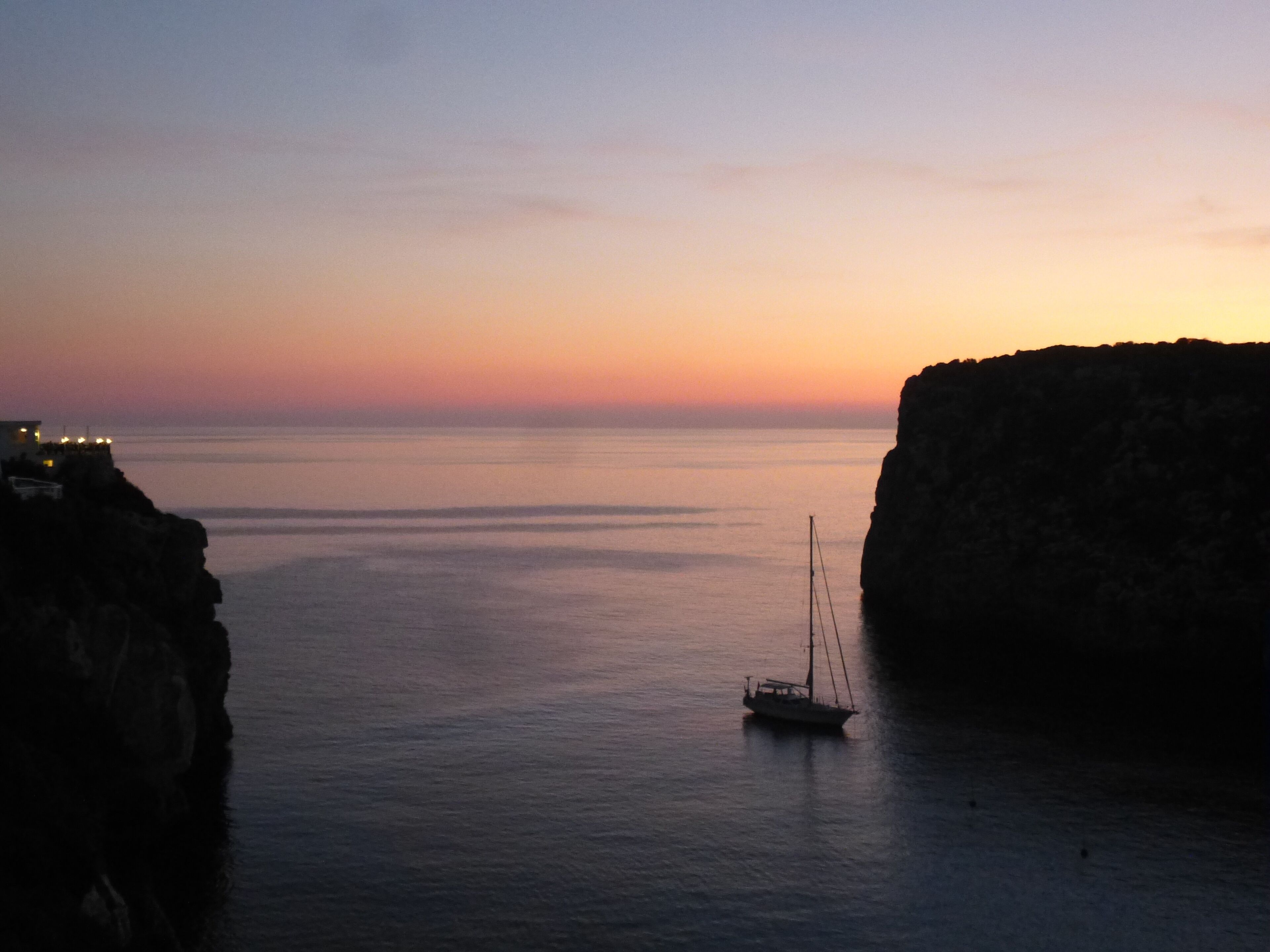 Un bateau sur des eaux calmes, près d’une côte rocheuse, au coucher du soleil.