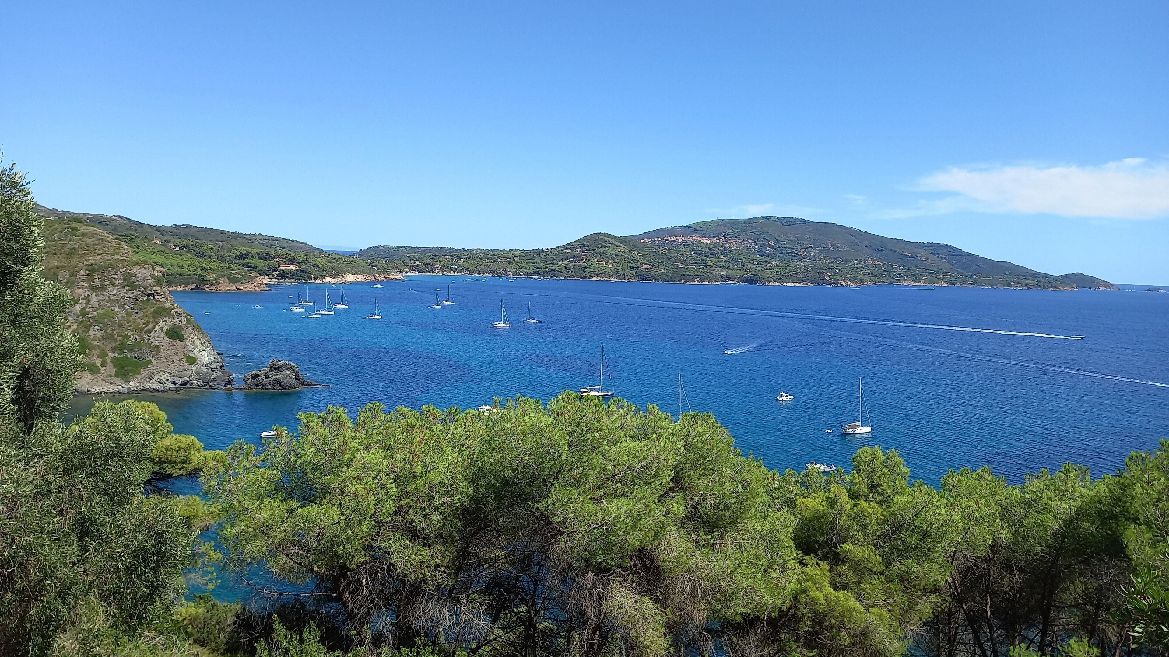 Paisaje costero con mar azul cristalino, barcos y colinas verdes.