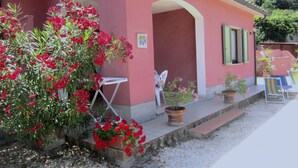 A house with a red exterior, a white door, and a small porch with two chairs and a table. - Villa Giuliana, bedroom for 4/5 Ptl. (Capoliveri)