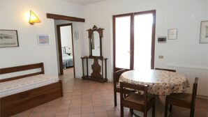 A room with a bed, a table with chairs, a mirror, and a door leading to another room. - Villa Giuliana, bedroom for 4/5 Ptl. (Capoliveri)