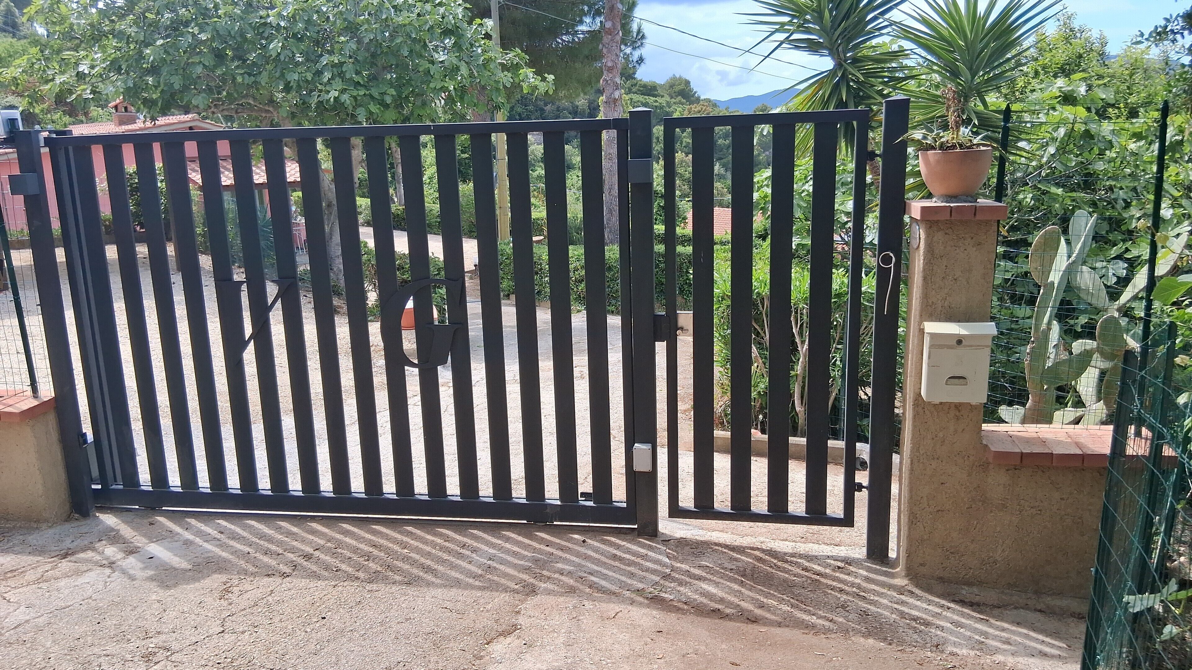 Una entrada tancada amb una reixa metàl·lica, un mur de formigó i una planta en test.