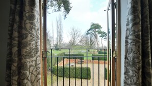 A view through a gate into a well-maintained garden with neatly trimmed hedges and a gravel path.