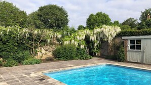 A rectangular swimming pool with clear blue water, surrounded by stone tiles.