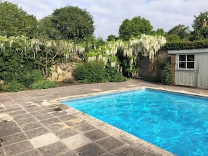 A rectangular swimming pool with clear blue water, surrounded by stone tiles.