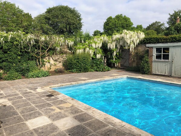 A rectangular swimming pool with clear blue water, surrounded by stone tiles.