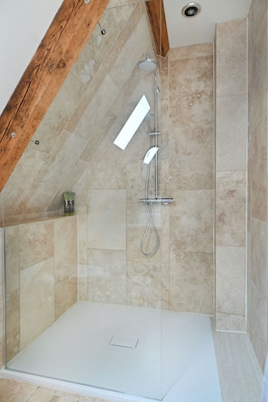 A shower with a glass door, a wooden ceiling beam, and beige tiled walls.