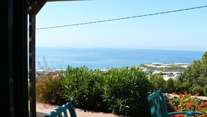 Vista da un balcone con tavolo e sedie, affaccio su un paesaggio costiero con vegetazione e cielo sereno.