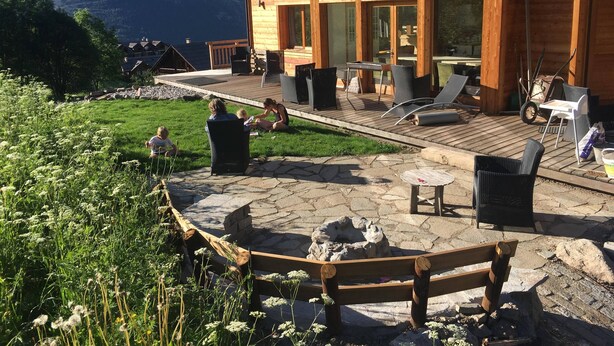 A wooden lodge with a deck, outdoor seating, and a view of mountains.