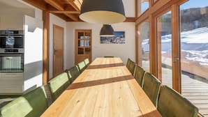 A wooden dining table with chairs, a modern kitchen, and large windows with a snowy view.