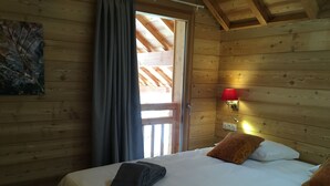 A wooden cabin room with a bed, towels, a red lamp, and a painting on the wall.