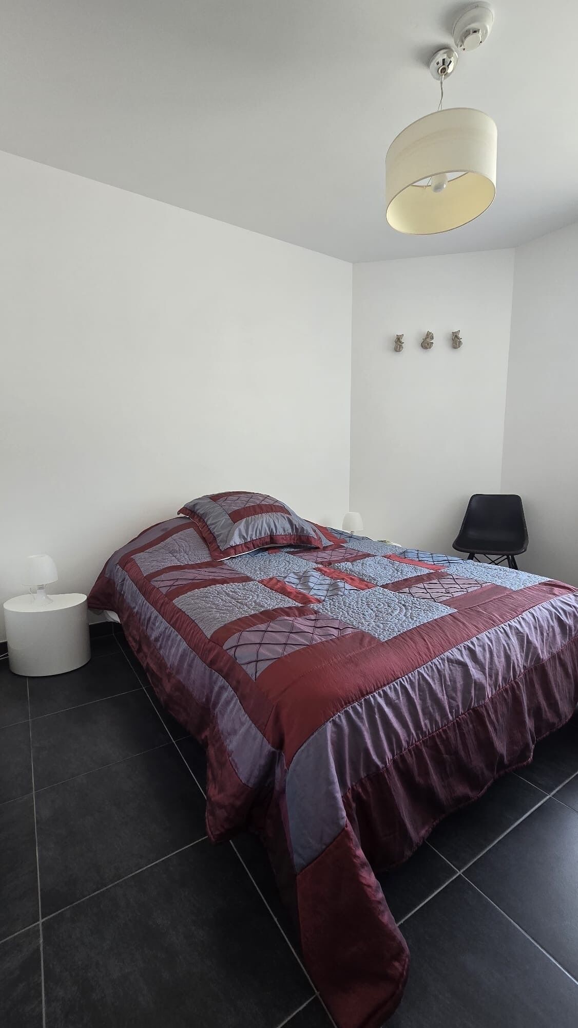 A bedroom with a bed, a chair, a nightstand, and a wall-mounted light fixture.