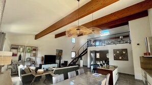 A spacious living area with a high ceiling, a dining table, sofas, and a staircase leading to an upper level. - Villa PALOMA PISCINE Chauffée SPA between Narbonne and Béziers- 15 km VALRAS PLAGE (Colombiers)