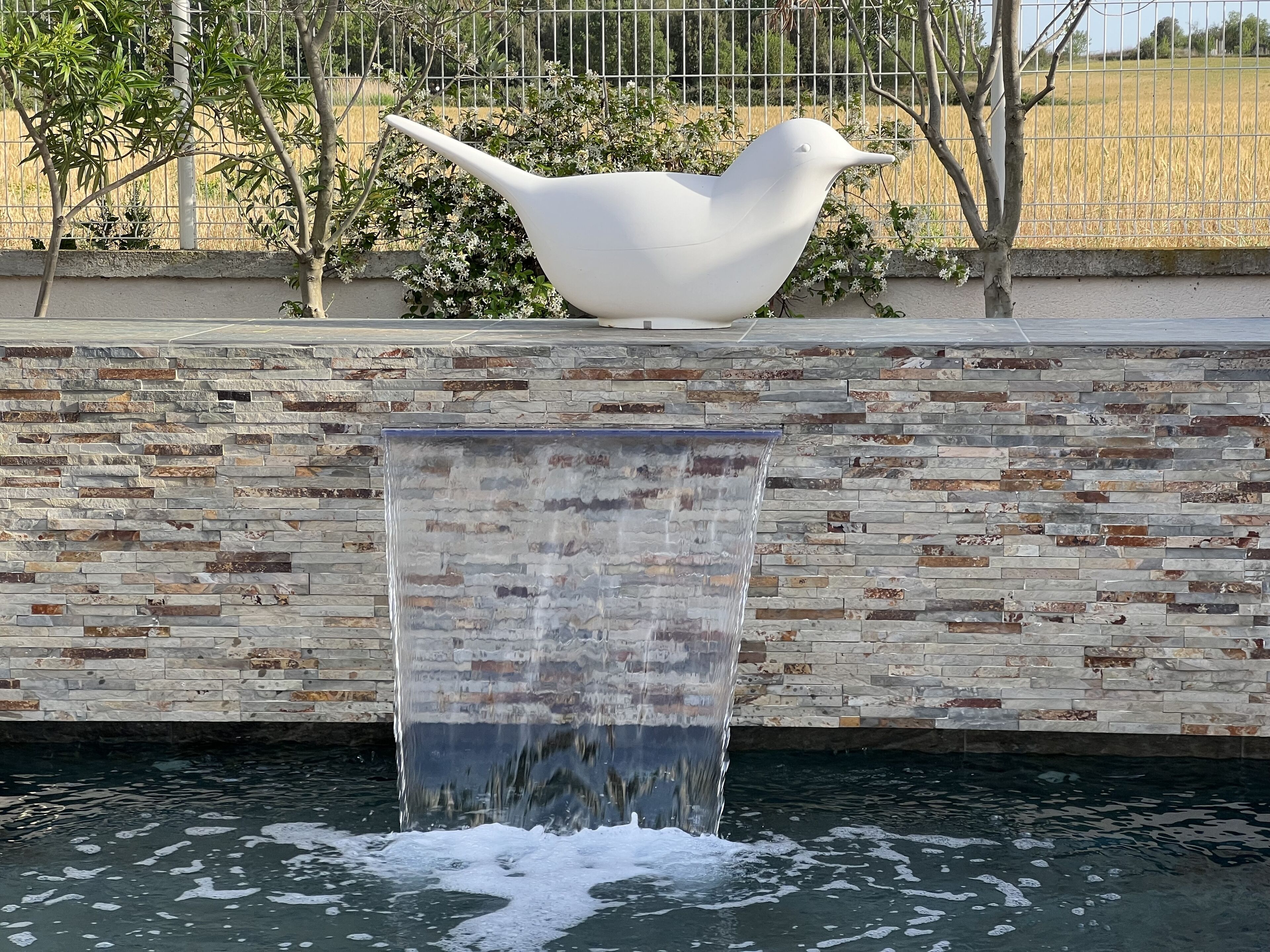 A bird-shaped water feature with a stone wall backdrop.