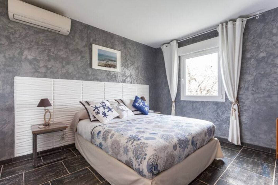 Een slaapkamer met een bed, nachtkastje, lamp, raam met gordijnen en een foto aan de muur.