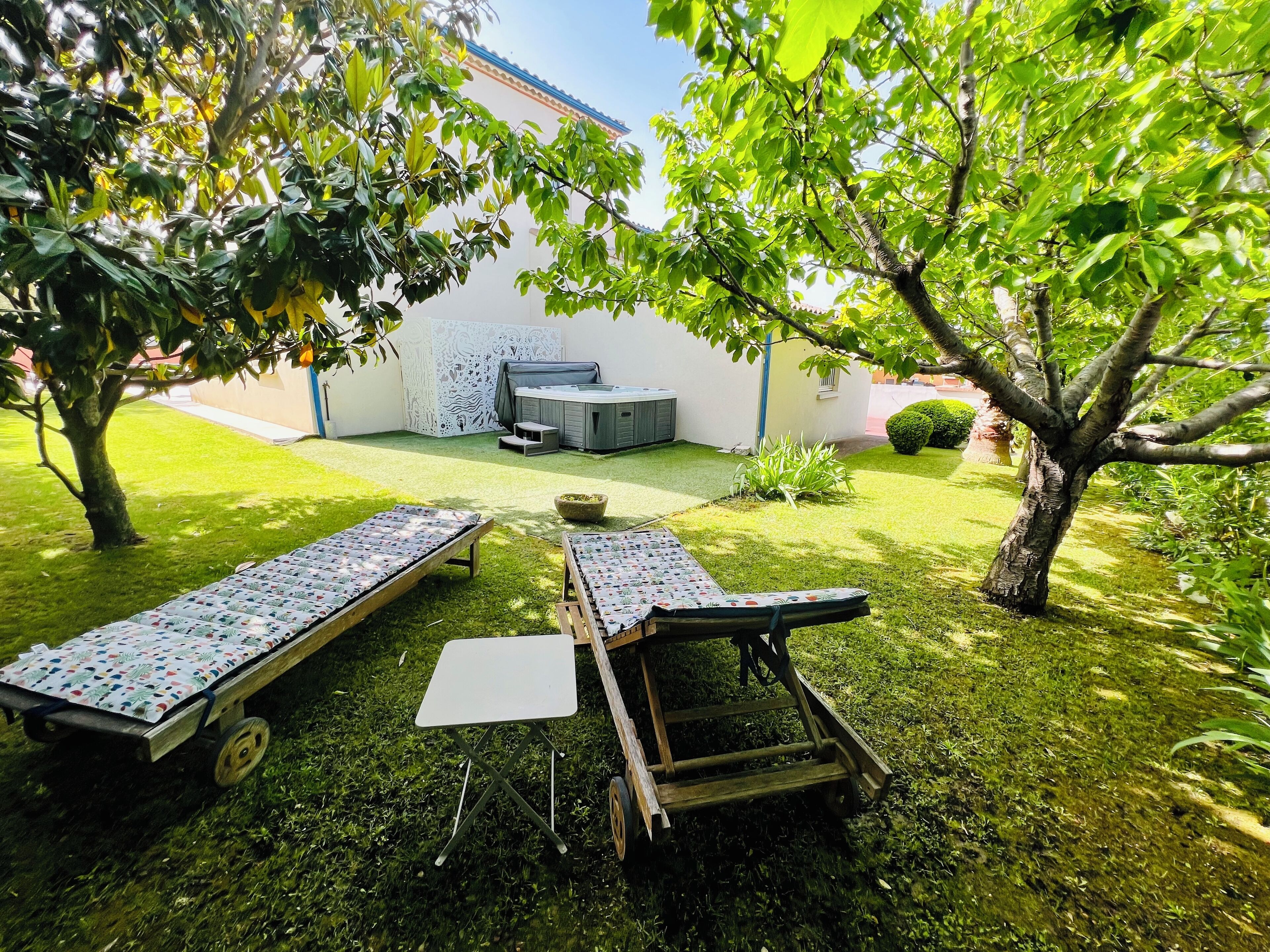Un patio trasero con dos tumbonas, un jacuzzi y una mesita.