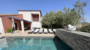 A swimming pool with lounge chairs, a stone wall, and a building with a balcony. - Villa PALOMA PISCINE Chauffée SPA between Narbonne and Béziers- 15 km VALRAS PLAGE (Colombiers)