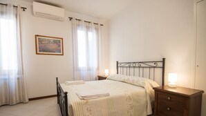 Une chambre à coucher comprenant un lit, des tables de chevet, une commode, un climatiseur fixé au mur et un tableau encadré accroché au mur.