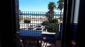 A balcony with a view of the beach, a table, chairs, and a railing.