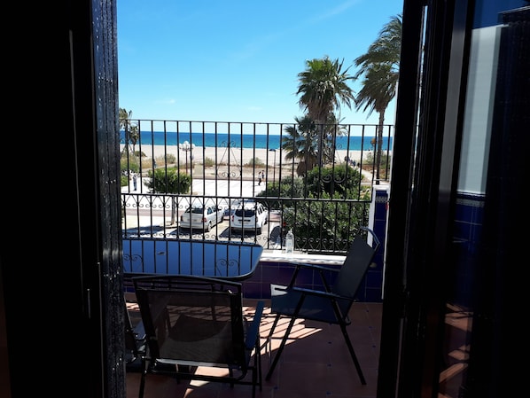 A balcony with a view of the beach, a table, chairs, and a railing.