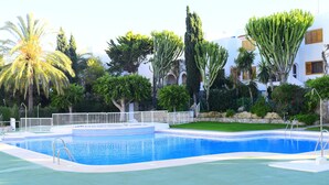 A swimming pool with a white deck, surrounded by various trees and a building with balconies.