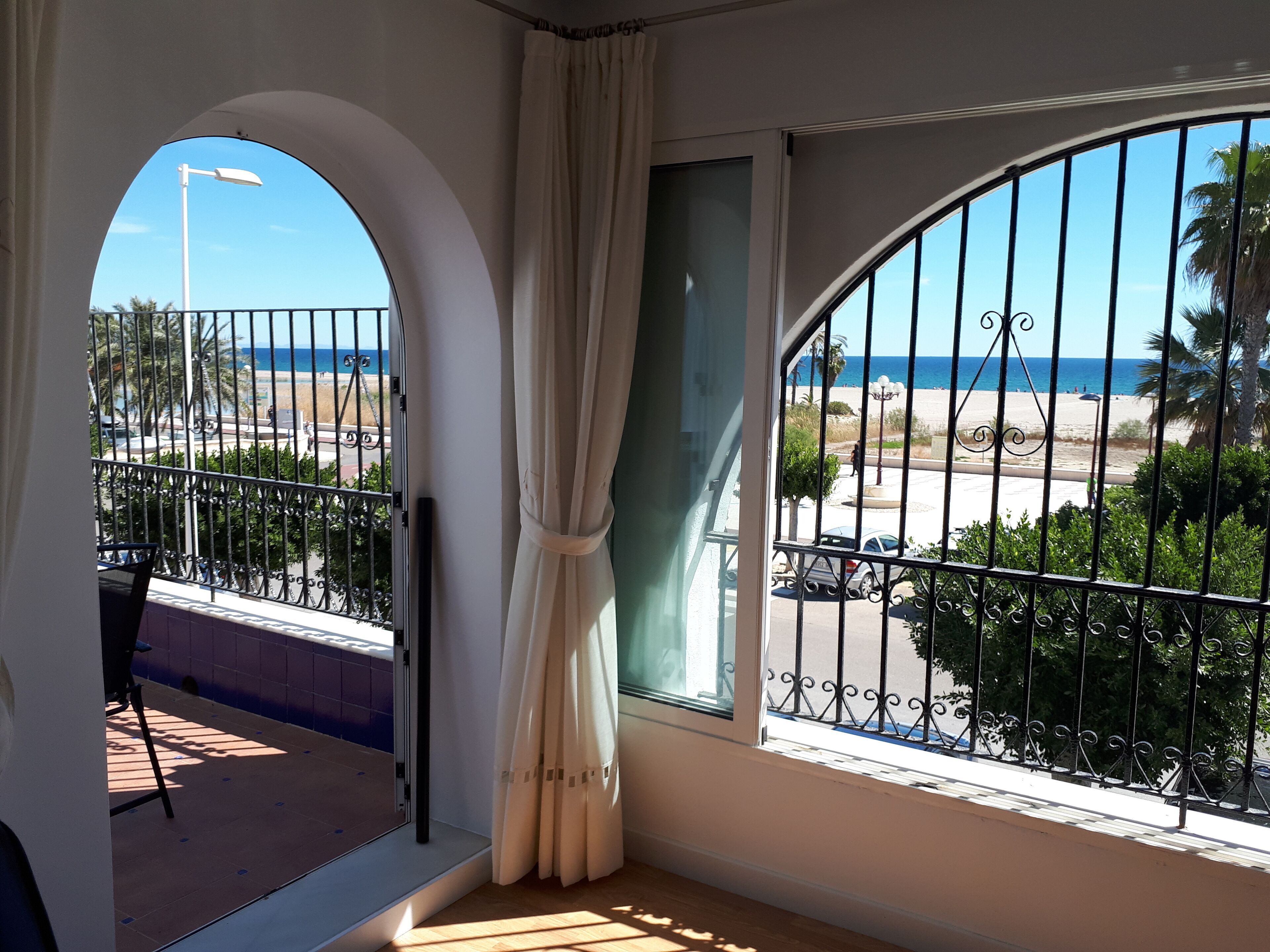 A balcony with a view of the beach, a metal railing, and a window with a curtain.