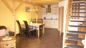 A cozy kitchen with a dining area, wooden beams, and a staircase. - VierJahreszeiten Appartments (Lübben (Spreewald))