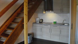 A kitchen with a wooden staircase, white cabinets, a sink, and a coffee maker. - VierJahreszeiten Appartments (Lübben (Spreewald))